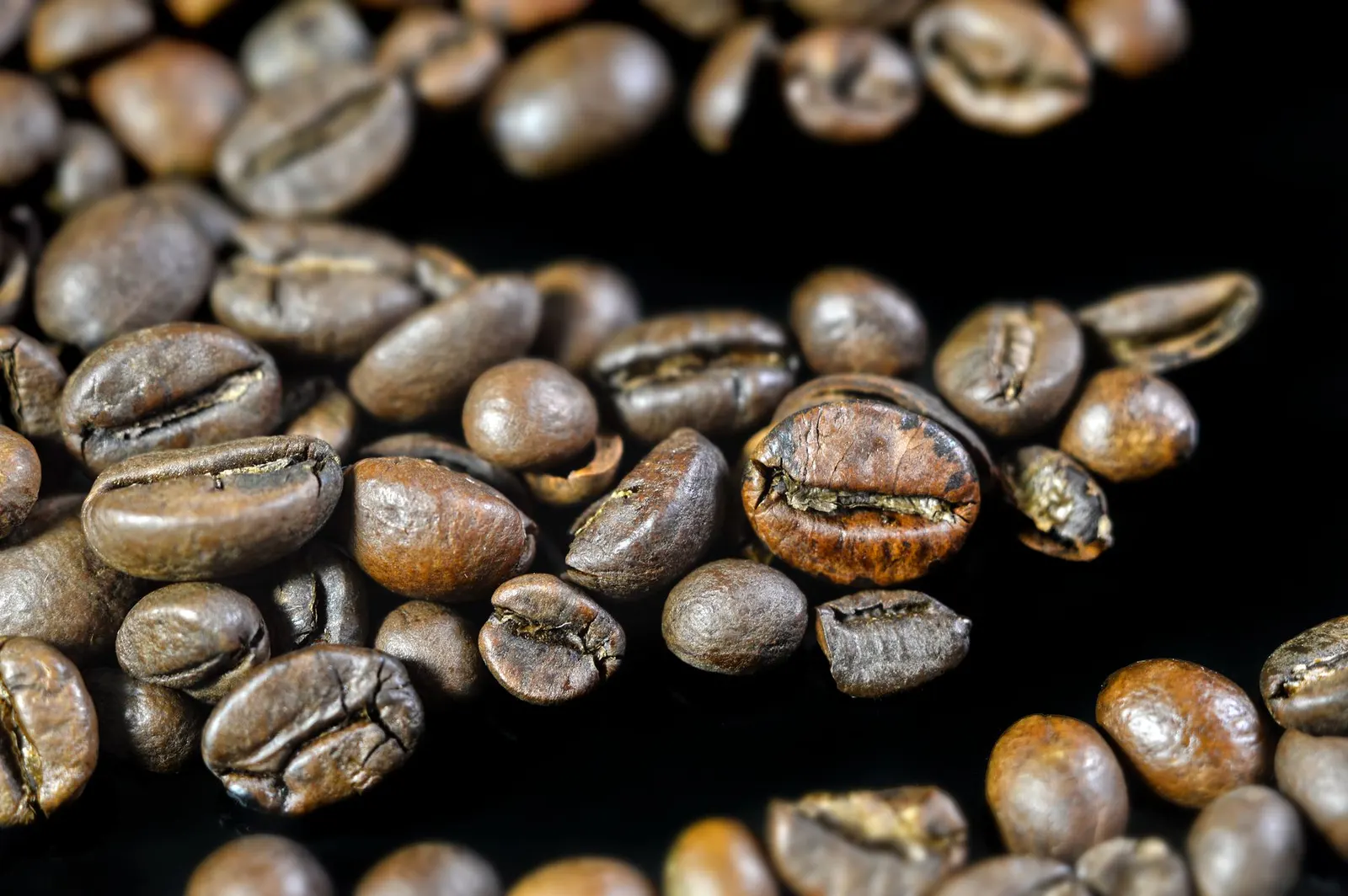 Macro view of dark roasted coffee beans, glossy and textured, on a black surface