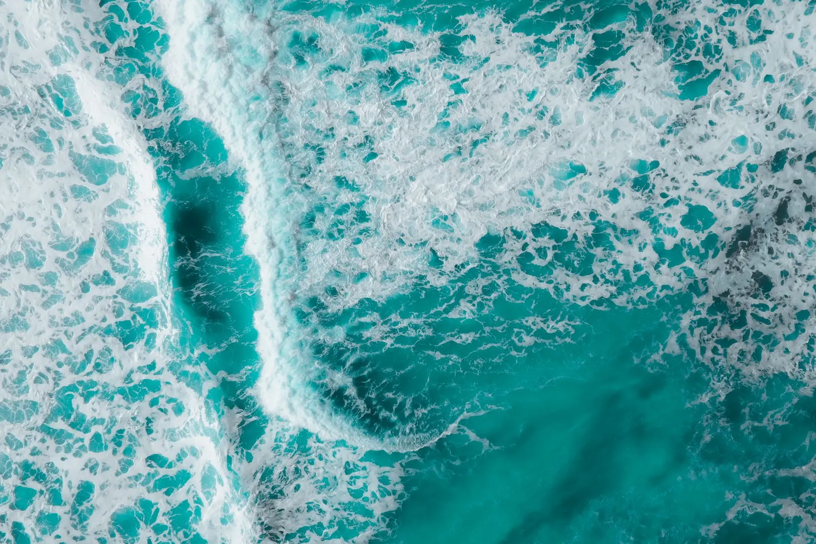 Captivating aerial shot of vibrant turquoise ocean waves crashing with foamy textures